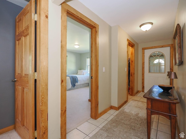 corridor with light tile patterned floors, baseboards, and light carpet