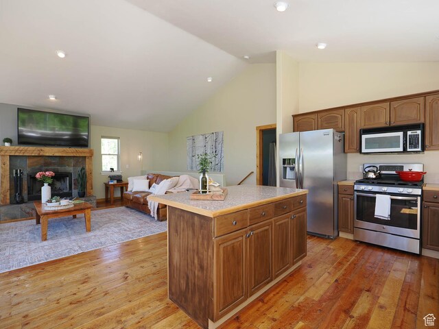 kitchen featuring a center island, light countertops, a tiled fireplace, stainless steel appliances, and light wood finished floors