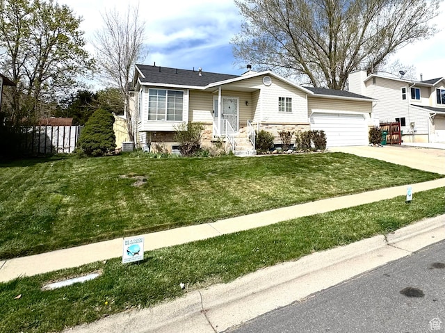 raised ranch featuring an attached garage, driveway, a front yard, and fence