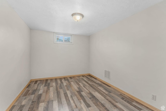 spare room featuring a textured ceiling, wood finished floors, baseboards, and visible vents