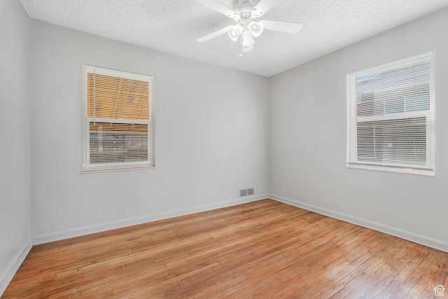 unfurnished room featuring baseboards, a textured ceiling, visible vents, ceiling fan, and light wood finished floors