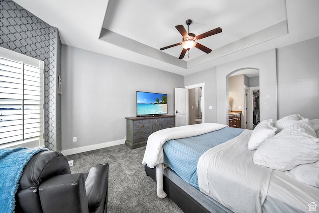 carpeted bedroom with baseboards, a raised ceiling, arched walkways, and connected bathroom