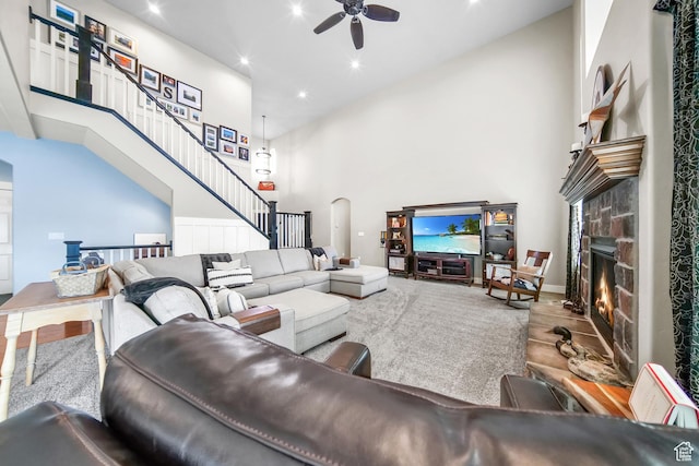 living area with arched walkways, a ceiling fan, a fireplace, a towering ceiling, and stairs