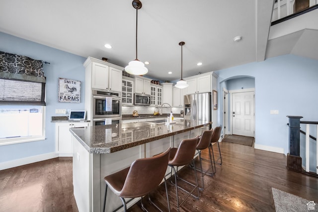 kitchen featuring tasteful backsplash, arched walkways, dark wood finished floors, white cabinetry, and stainless steel appliances