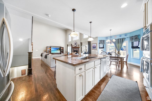 kitchen featuring appliances with stainless steel finishes, white cabinets, a brick fireplace, dark wood finished floors, and a sink