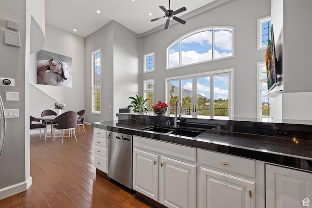 kitchen with stainless steel dishwasher, dark wood-style flooring, a sink, and dark countertops