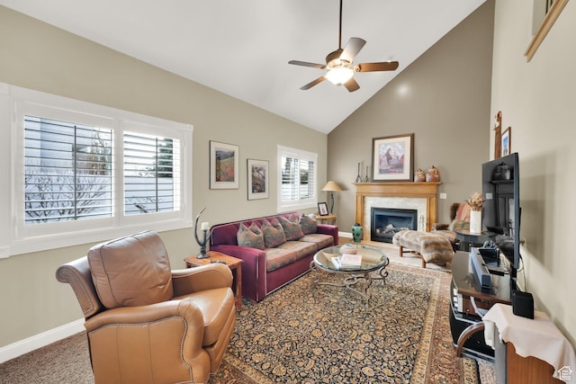 living area with high vaulted ceiling, a ceiling fan, a glass covered fireplace, carpet flooring, and baseboards