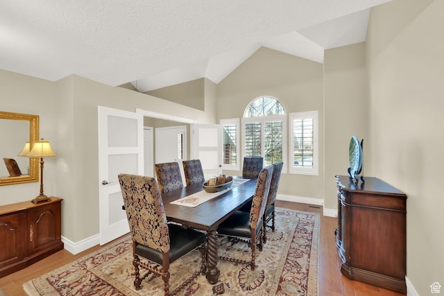 dining area with light wood-style flooring, a textured ceiling, baseboards, and vaulted ceiling