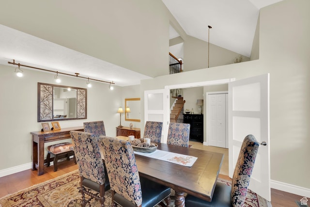 dining area featuring track lighting, wood finished floors, high vaulted ceiling, and baseboards