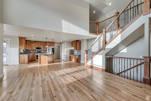 1135 Grandview Dr, Providence, UT 84332 - unfurnished living room featuring light wood-style flooring, recessed lighting, a towering ceiling, and stairway