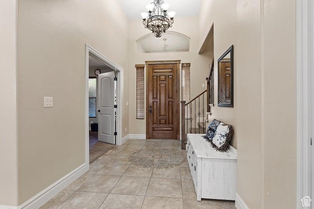 entryway featuring baseboards, a chandelier, light tile patterned floors, a high ceiling, and stairs
