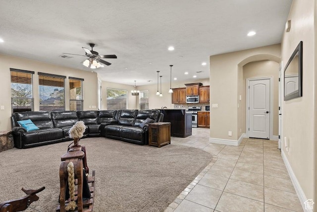 living area featuring light tile patterned flooring, arched walkways, ceiling fan, and plenty of natural light