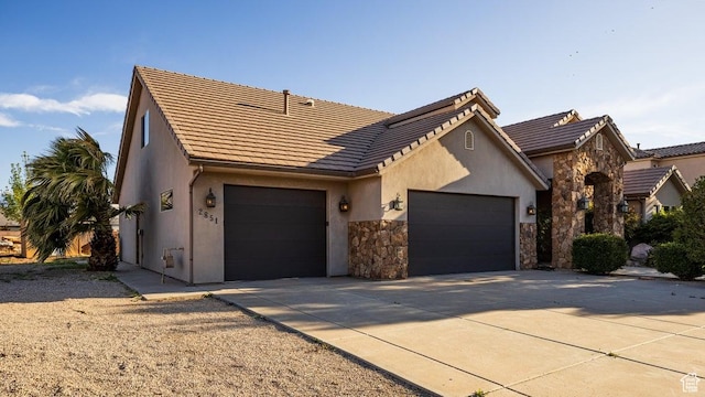 view of front facade featuring stucco siding, driveway, stone siding, a tile roof, and a garage