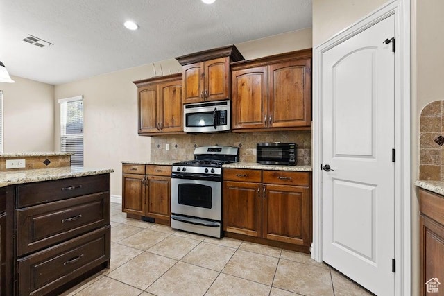 kitchen with light stone counters, light tile patterned floors, backsplash, visible vents, and stainless steel appliances