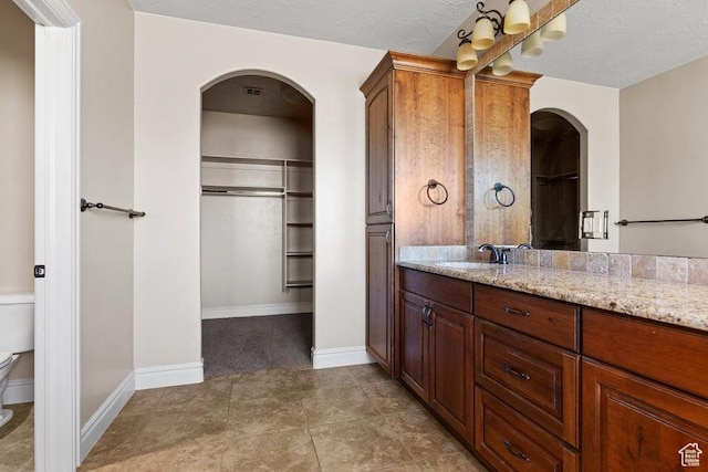 bathroom featuring a textured ceiling, vanity, toilet, a walk in closet, and baseboards