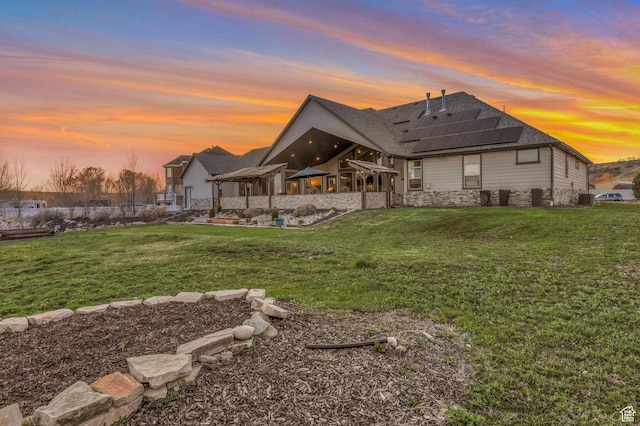 1737 E 6850 S, Uintah, UT 84405 - back of house at dusk with solar panels, stone siding, roof with shingles, and a yard