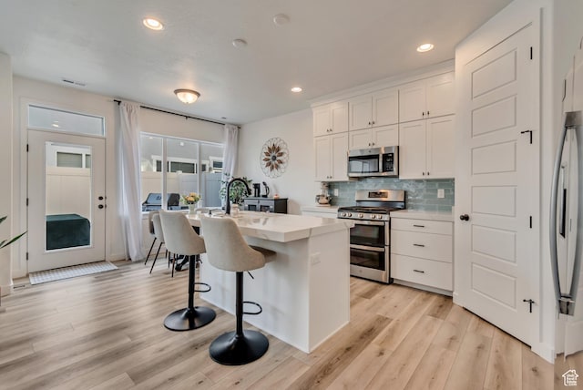 kitchen with a kitchen breakfast bar, tasteful backsplash, white cabinets, appliances with stainless steel finishes, and light wood finished floors