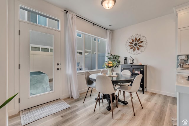 dining room with light wood-type flooring, a healthy amount of sunlight, and baseboards