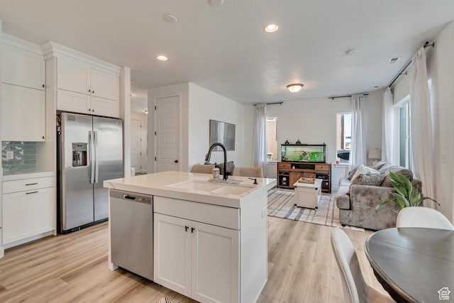 kitchen with a sink, open floor plan, light wood-style floors, white cabinetry, and stainless steel appliances