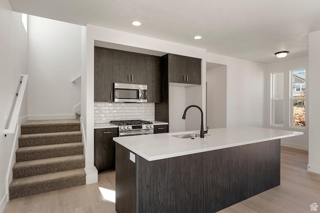 516 W Olive Ln, St George, UT 84790 - kitchen featuring appliances with stainless steel finishes, backsplash, light countertops, light wood-style floors, and an island with sink