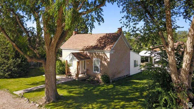 view of side of home with a chimney, a shingled roof, concrete block siding, and a lawn