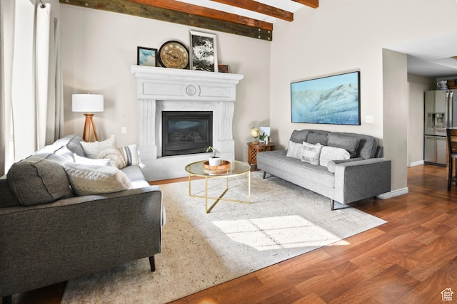 living area featuring a glass covered fireplace, baseboards, beamed ceiling, and wood finished floors
