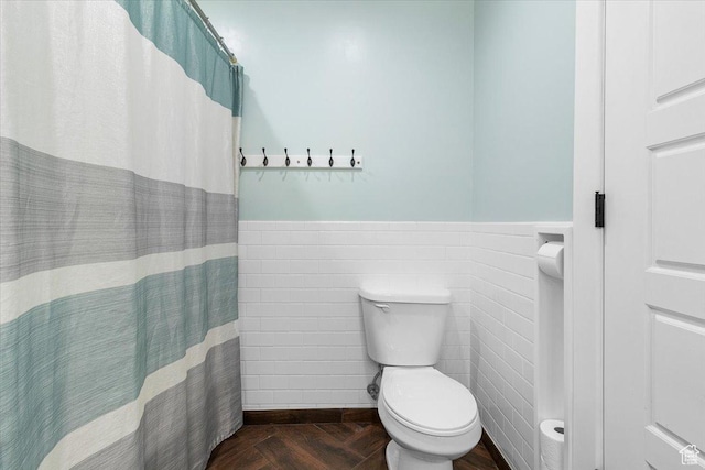 full bath with toilet, tile walls, curtained shower, and a wainscoted wall