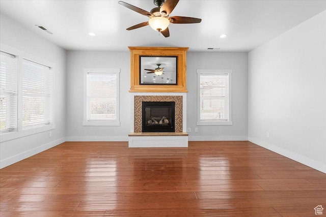 unfurnished living room with a tiled fireplace, a wealth of natural light, and hardwood / wood-style flooring
