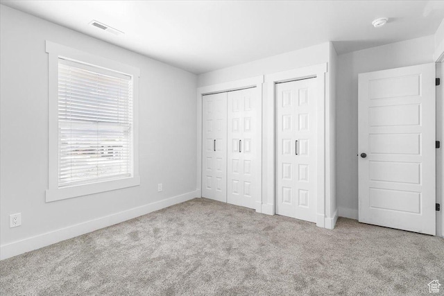 unfurnished bedroom with carpet, visible vents, baseboards, and multiple closets