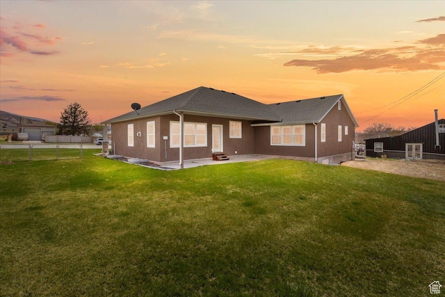 back of house at dusk featuring a patio area, stucco siding, fence, and a lawn