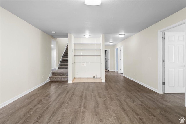 unfurnished living room featuring baseboards, stairway, wood finished floors, and built in shelves