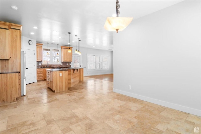 kitchen with tasteful backsplash, baseboards, a kitchen breakfast bar, freestanding refrigerator, and a kitchen island