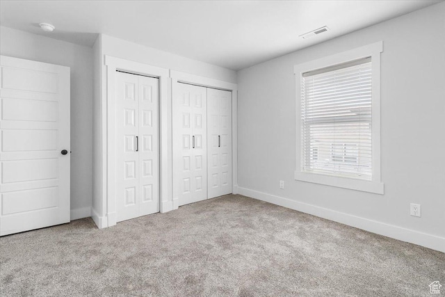 unfurnished bedroom featuring two closets, baseboards, visible vents, and carpet floors