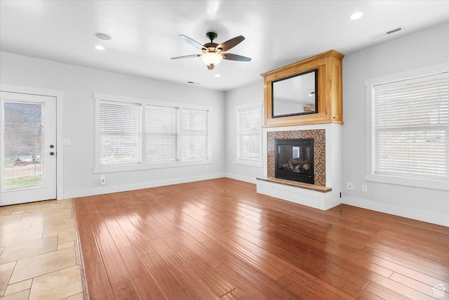 unfurnished living room with a healthy amount of sunlight, ceiling fan, a glass covered fireplace, and visible vents