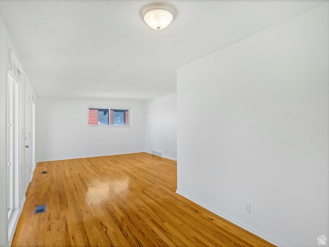 spare room with a textured ceiling, light wood finished floors, baseboards, and visible vents