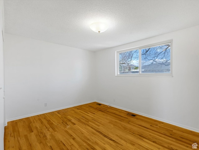 unfurnished room featuring light wood-style flooring, a textured ceiling, baseboards, and visible vents