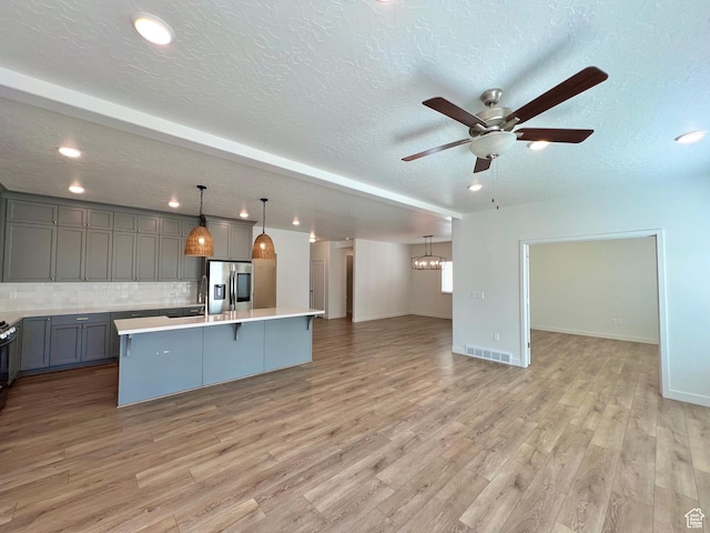 6293 W Jackson Crest Way, Herriman, UT 84096 - kitchen featuring gray cabinets, stainless steel fridge, open floor plan, light wood-style floors, and ceiling fan with notable chandelier