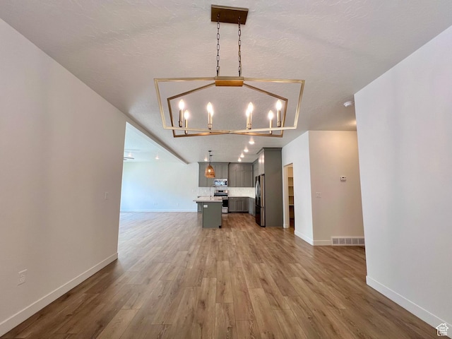 6293 W Jackson Crest Way, Herriman, UT 84096 - unfurnished living room with visible vents, baseboards, light wood-type flooring, and a notable chandelier