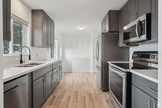 kitchen with light wood-type flooring, light countertops, a sink, and appliances with stainless steel finishes