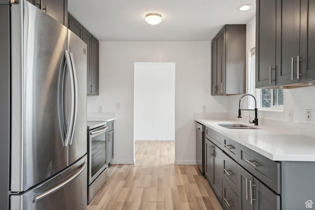 kitchen with baseboards, light wood-style flooring, light countertops, stainless steel appliances, and a sink