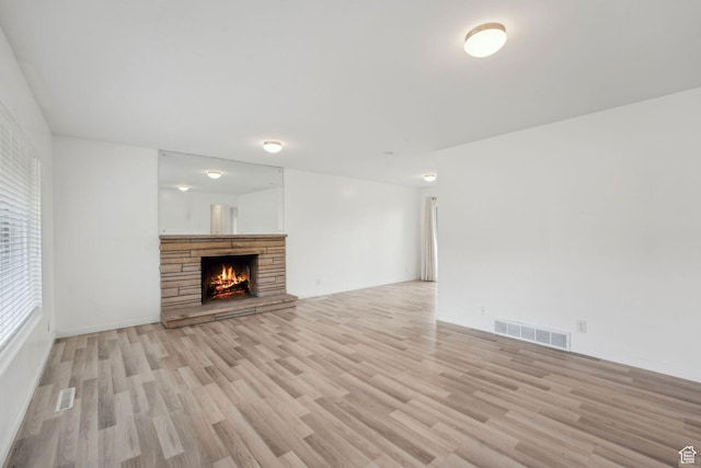 unfurnished living room featuring a stone fireplace, visible vents, and light wood-style flooring