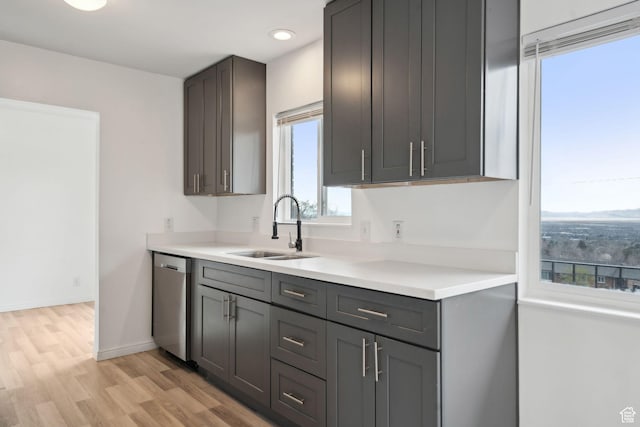 kitchen with light wood finished floors, dishwasher, light countertops, and a sink