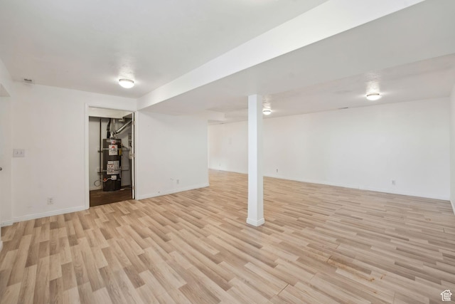 finished below grade area with light wood-style flooring, strapped water heater, and baseboards