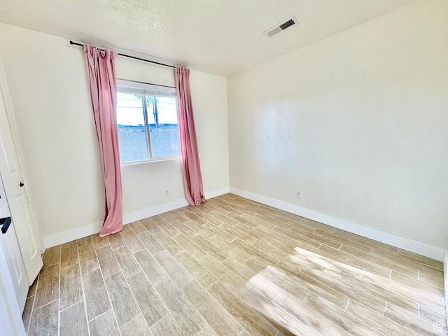 unfurnished room with a textured ceiling, visible vents, baseboards, and wood finish floors