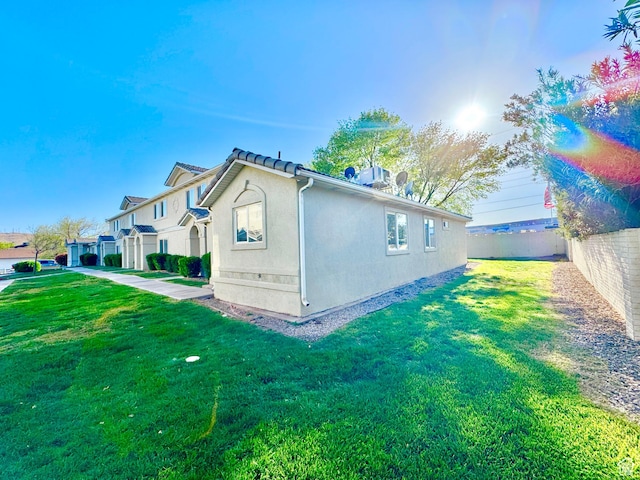 view of side of home featuring stucco siding, fence, and a lawn