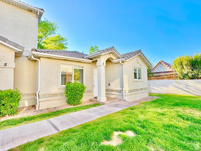 view of front of home with a tiled roof, a front yard, fence, and stucco siding