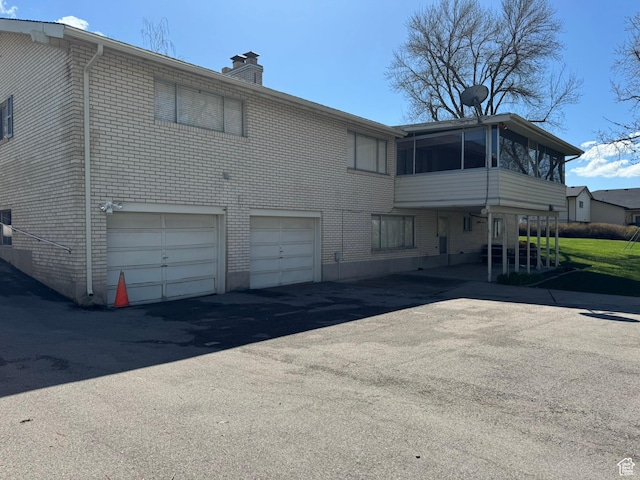 871 N Bonita Way E Unit 19, Centerville, UT 84014 - back of house featuring a sunroom, an attached garage, aphalt driveway, a chimney, and brick siding