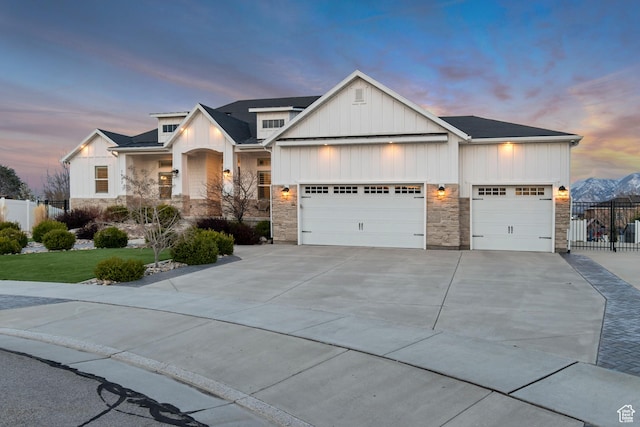 view of front of house featuring concrete driveway, stone siding, board and batten siding, a garage, and fence