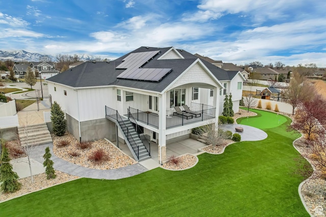 back of house with solar panels, fence, stairs, a residential view, and roof with shingles