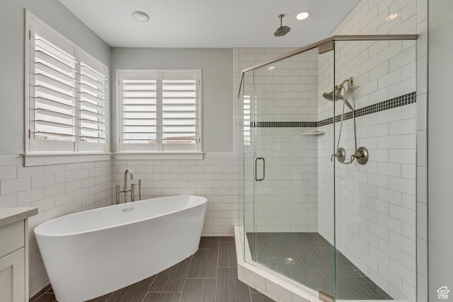 bathroom featuring a shower stall, a freestanding tub, vanity, wainscoting, and tile walls